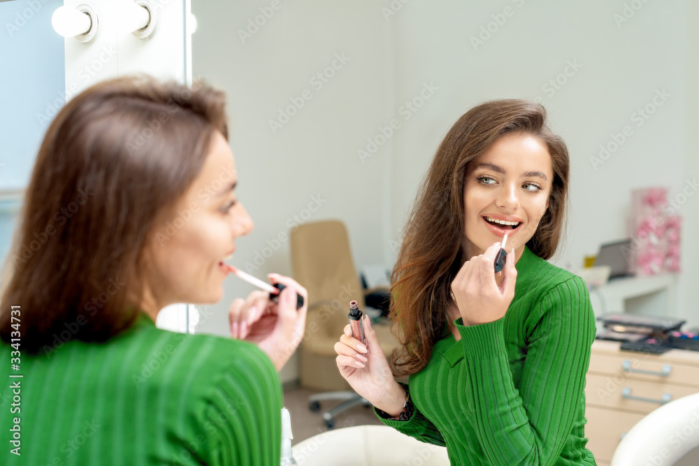 Beautiful young woman applies lipstick on her lips looking in mirror. Beautiful young woman applies lipstick on her lips looking in mirror.