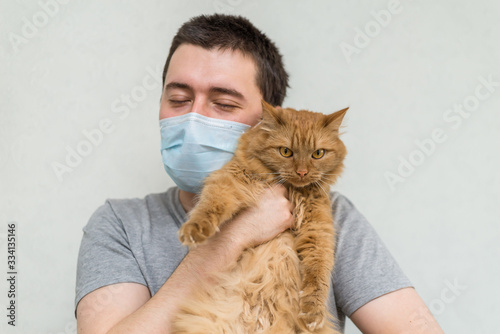 a man in a medical mask holds a pet cat.  Pets during a pandemic, the coronavirus and influenza. without leaving the house © Асель Иржанова