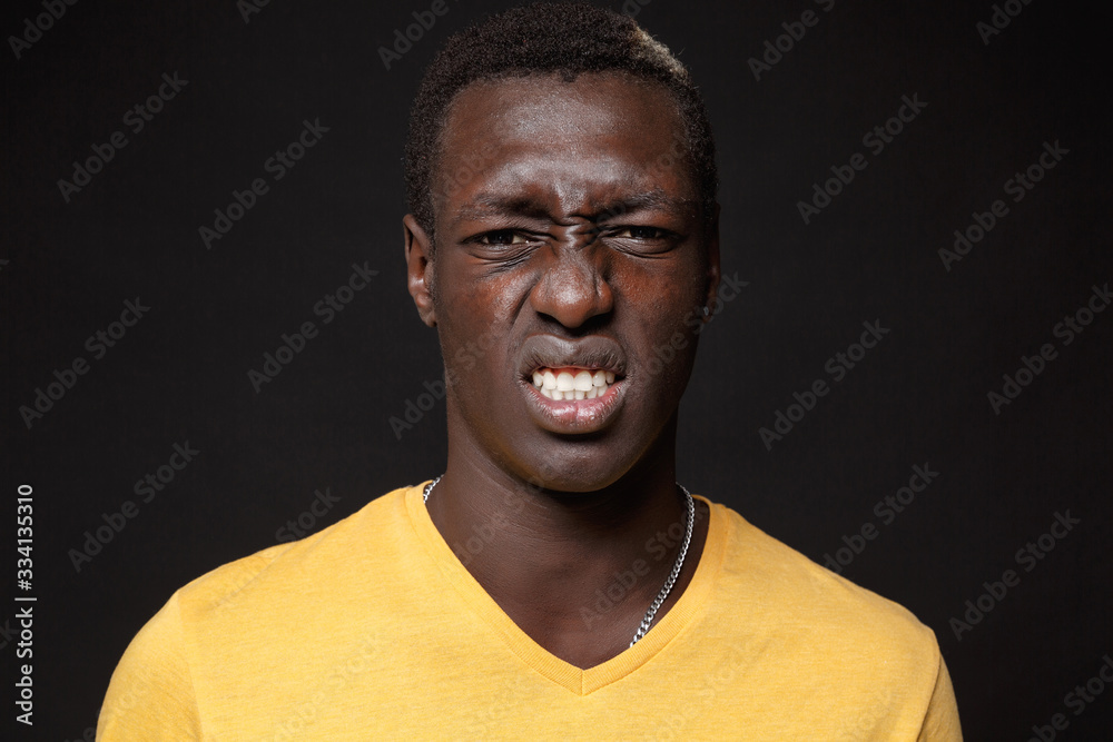 Close up of displeased disgusted young african american man guy in yellow t-shirt posing isolated on black background studio portrait. People lifestyle concept. Mock up copy space. Looking camera.