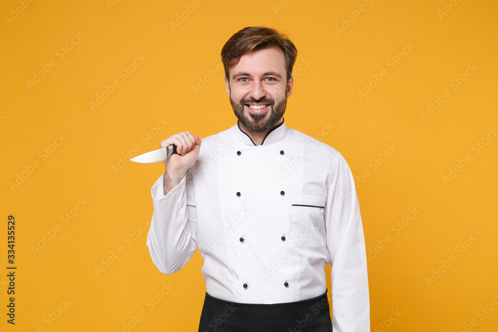 Smiling crazy young bearded male chef cook or baker man in white uniform shirt posing isolated on yellow wall background studio portrait. Cooking food concept. Mock up copy space. Holding knife. Smiling crazy young bearded male chef cook or baker man in white uniform shirt posing isolated on yellow wall background studio portrait. Cooking food concept. Mock up copy space. Holding knife.
