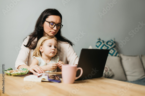 Woman works at home on a laptop with a child. Mom works remotely at home. Lifestyle photos.