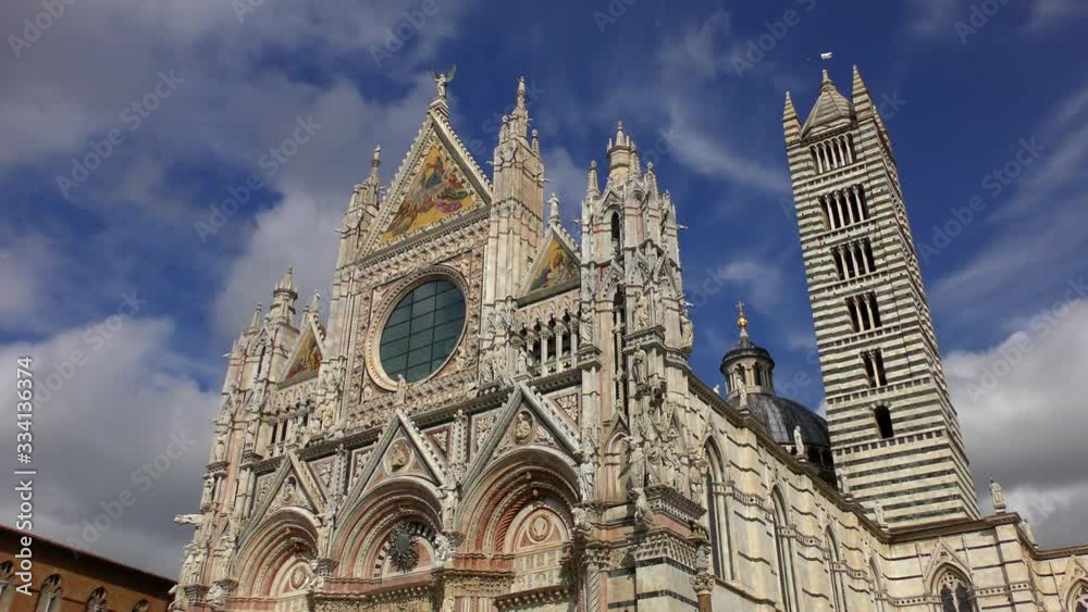 The facade and tower of the Duomo Cathedral in Siena against the background of clouds rapidly moving across the sky. The facade and tower of the Duomo Cathedral in Siena against the background of clouds rapidly moving across the sky.