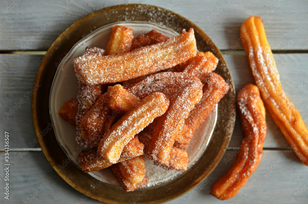 Churros sprinkled with powdered sugar on a plate on a wooden background Churros sprinkled with powdered sugar on a plate on a wooden background