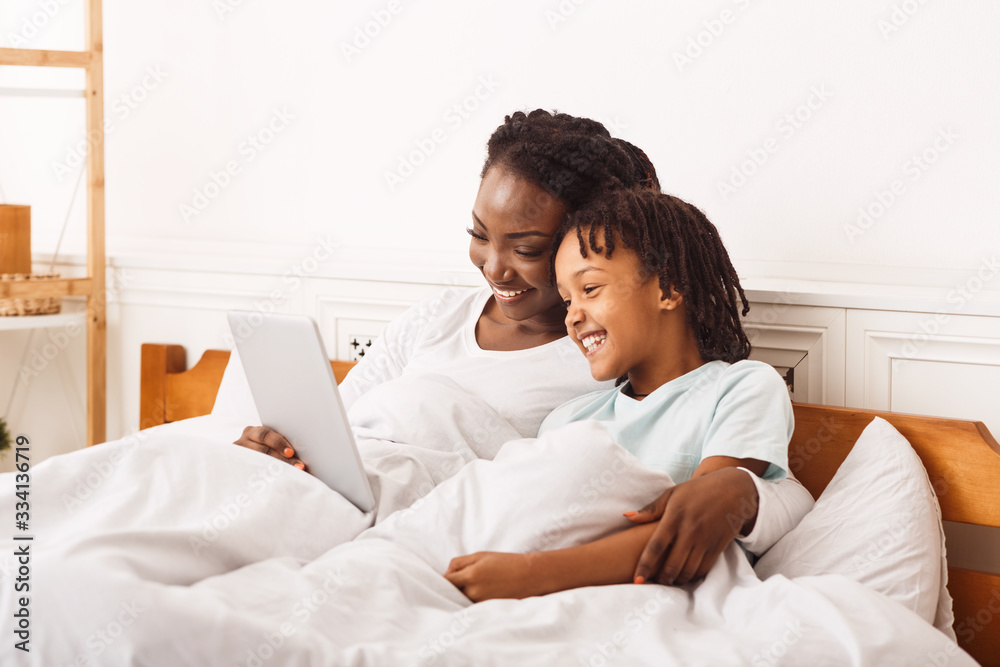 Black mother watching cartoons with her daughter in bed Black mother watching cartoons with her daughter in bed
