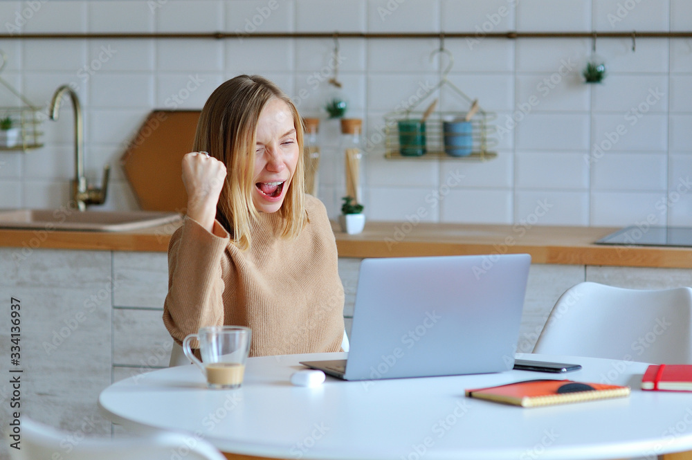 Lovely blonde woman working with her laptop while sitting in the kitchen in her apartment Lovely blonde woman working with her laptop while sitting in the kitchen in her apartment