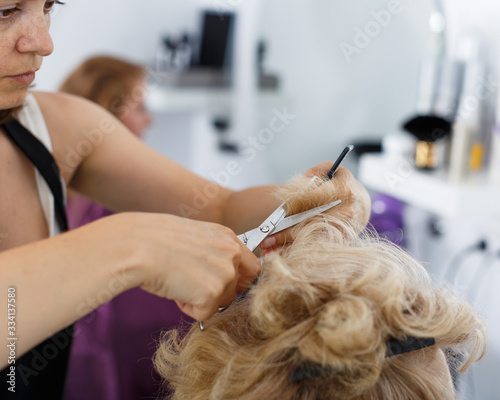 Hands of hairdresser making hairstyle for female