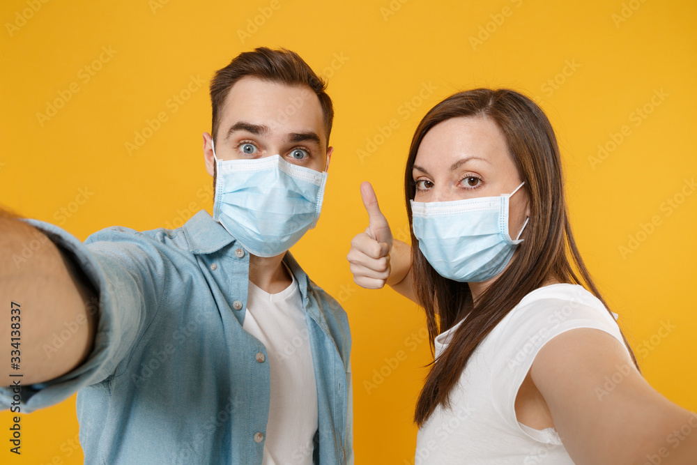Two people in sterile face masks white t-shirts isolated on yellow background studio. Epidemic pandemic rapidly spreading coronavirus 2019-ncov medicine flu virus ill sick disease treatment concept.