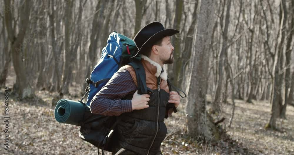 Middle aged bearded male tourist walking in forest and looking around, enjoying scenery Middle aged bearded male tourist walking in forest and looking around, enjoying scenery