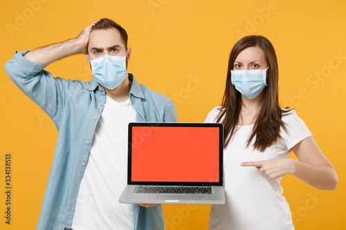 Two people in sterile face masks using laptop pc isolated on yellow background studio. Epidemic pandemic rapidly spreading coronavirus 2019-ncov medicine flu virus ill sick disease treatment concept.