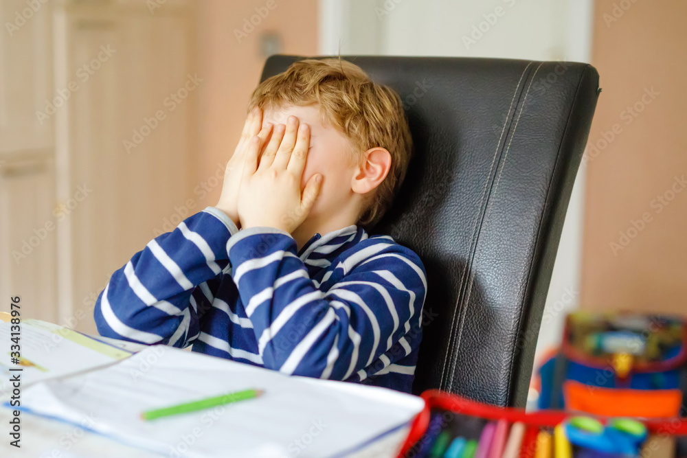 Upset school kid boy making homework during quarantine time from corona pandemic disease. Crying and sad boy frustrating staying at home. Homeschooling concept Upset school kid boy making homework during quarantine time from corona pandemic disease. Crying and sad boy frustrating staying at home. Homeschooling concept