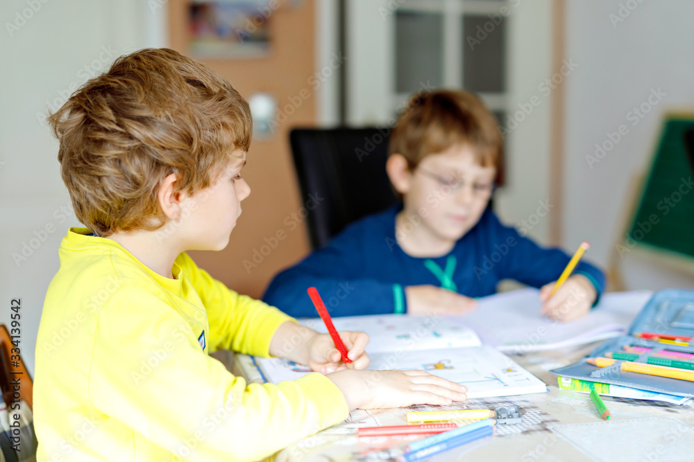 Two hard-working school kids boys making homework during quarantine time from corona pandemic disease. Children, brothers writing with pen, staying at home. Homeschooling concept. Two hard-working school kids boys making homework during quarantine time from corona pandemic disease. Children, brothers writing with pen, staying at home. Homeschooling concept.