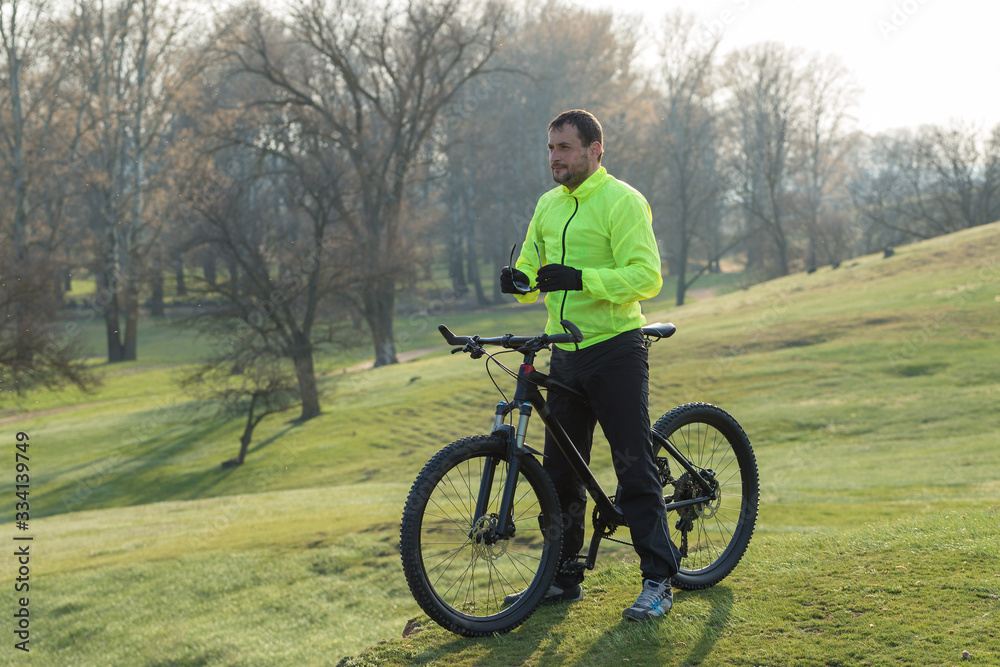 Fototapeta premium Cyclist in pants and green jacket on a modern carbon hardtail bike with an air suspension fork. The guy on the top of the hill rides a bike.