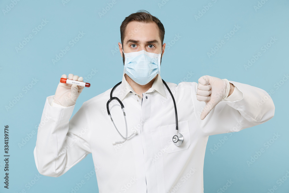 Male doctor man in gown face mask gloves isolated on blue background. Epidemic pandemic coronavirus 2019-ncov sars covid-19 flu virus concept. Hold blood test result Sample tube showing thumb down. Male doctor man in gown face mask gloves isolated on blue background. Epidemic pandemic coronavirus 2019-ncov sars covid-19 flu virus concept. Hold blood test result Sample tube showing thumb down.