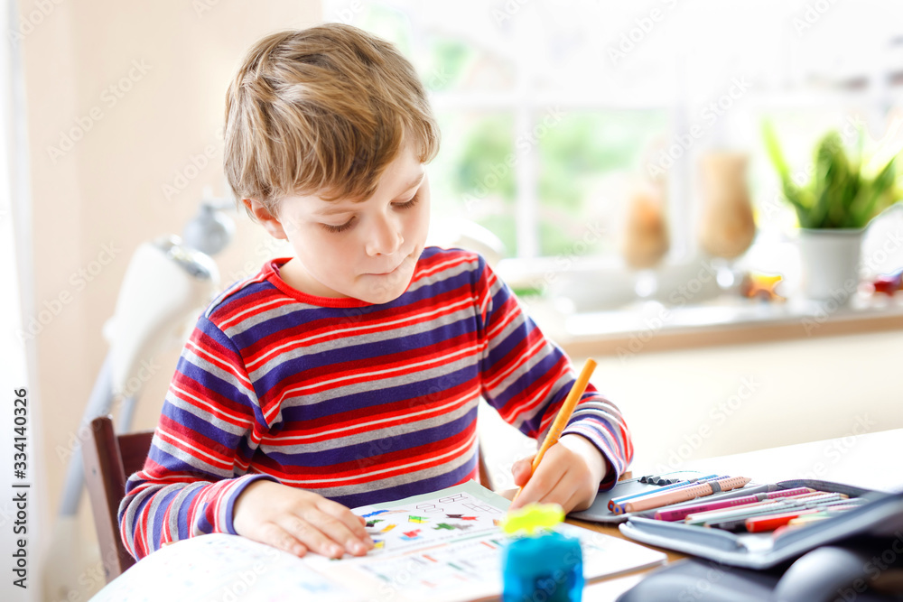 Hard-working happy school kid boy making homework during quarantine time from corona pandemic disease. Healthy child writing with pen, staying at home. Homeschooling concept Hard-working happy school kid boy making homework during quarantine time from corona pandemic disease. Healthy child writing with pen, staying at home. Homeschooling concept