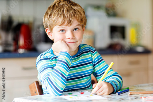 Hard-working happy school kid boy making homework during quarantine time from corona pandemic disease. Healthy child writing with pen, staying at home. Homeschooling concept photo