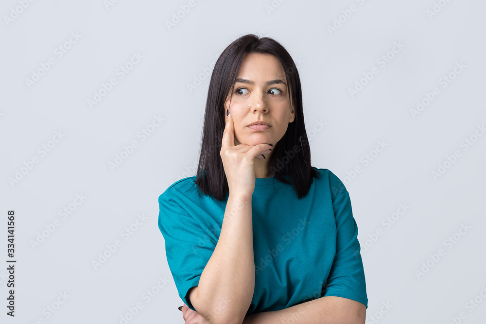 Portrait of a beautiful girl in a blue t-shirt, looks aside with pensive expression, is considering a plan for further action.