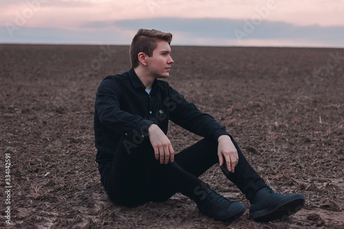  Young man in black in the field. Pink sunset. Serious businessman