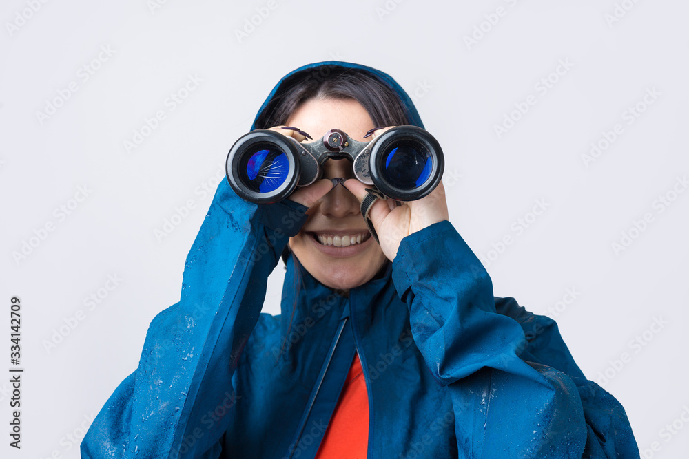 A tourist girl in a blue raincoat holds binoculars in her hands and looks into the distance, spies. A tourist girl in a blue raincoat holds binoculars in her hands and looks into the distance, spies.