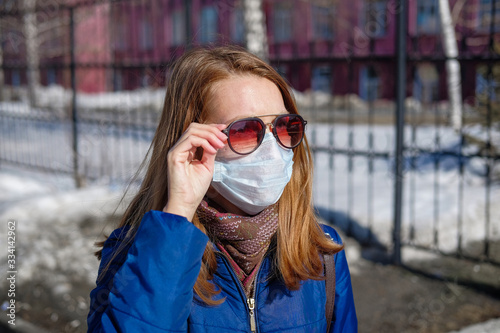 A woman in a medical mask walks alone on the street during the quarantine. Portrait of a female in a protective face mask against coronavirus.