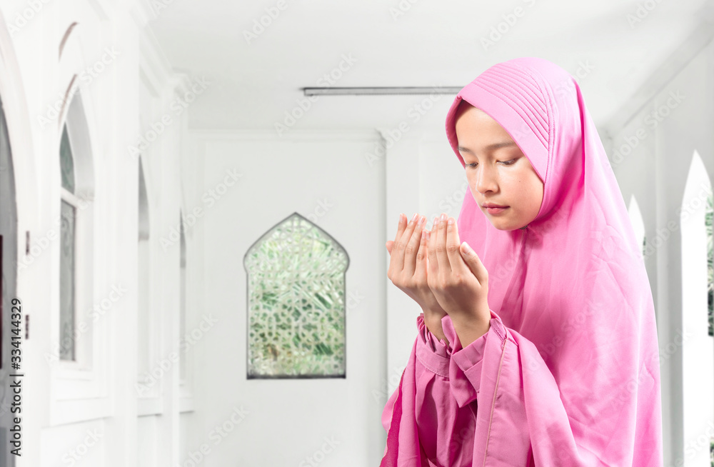 Asian Muslim woman in a veil standing while raised hands and praying