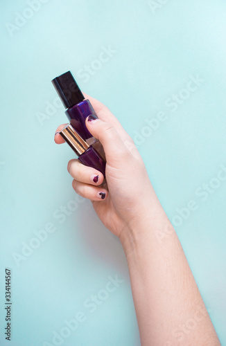 Close-up of hand with awful manicure holds bottle of nail polish on light background