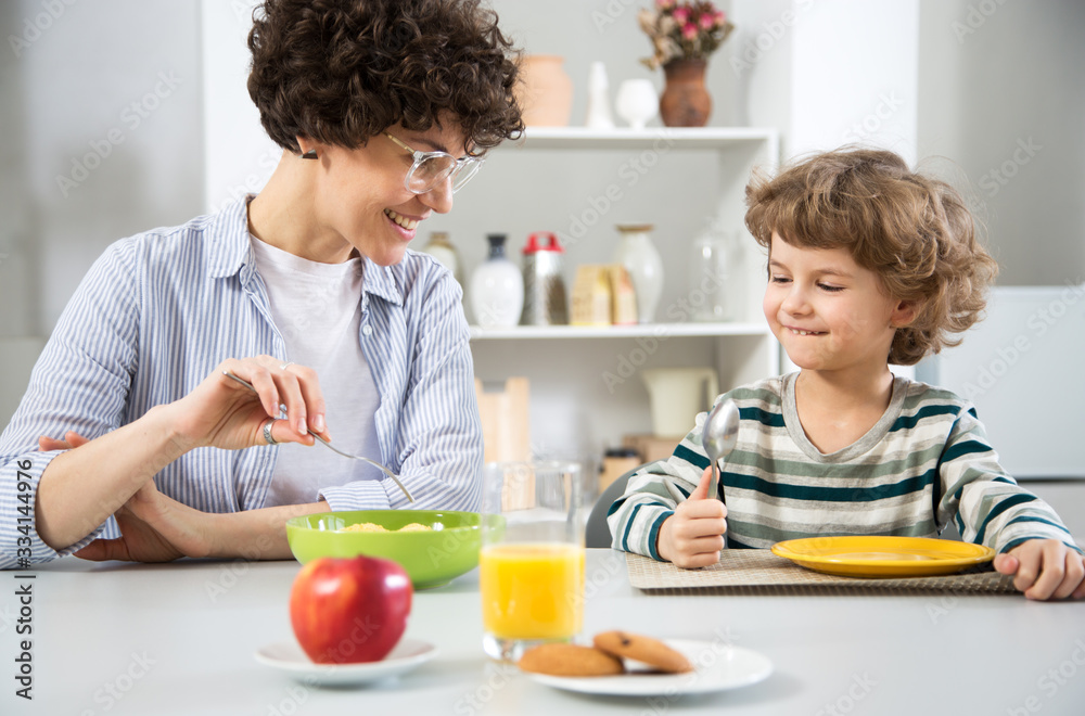 Woman and her cute little son are have breakfast and smiling together