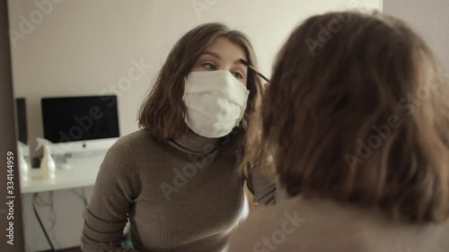 Young girl in a protective mask does makeup in front of a mirror while sitting at home in quarantine.Coronavirus. COVID-19 photo