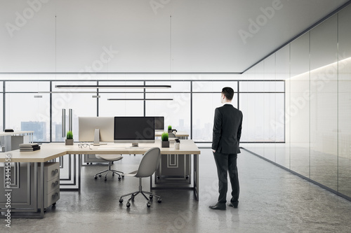 Businessman standing in office interior with city view and daylight.