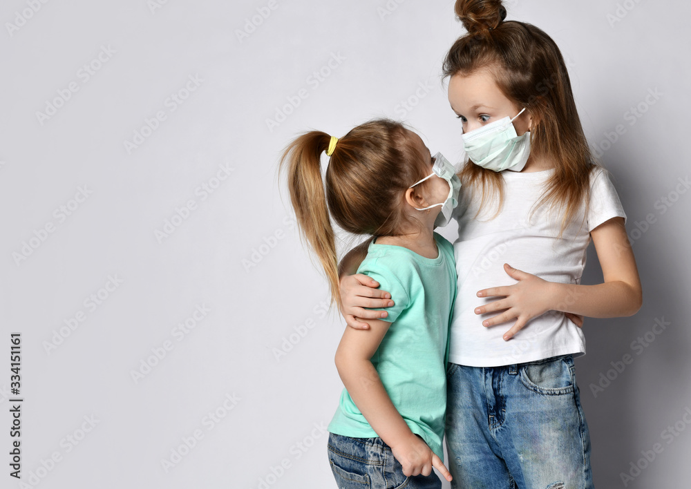 Two little girls wearing medical masks for protecting health from coronavirus epidemic, standing and looking at each Two little girls wearing medical masks for protecting health from coronavirus epidemic, standing and looking at each