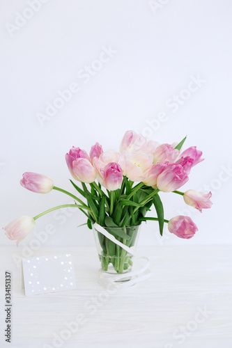Tulip flowers in glass vase with gift card over white background isolated