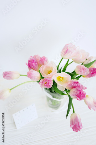 Tulip flowers in glass vase with gift card over white background isolated