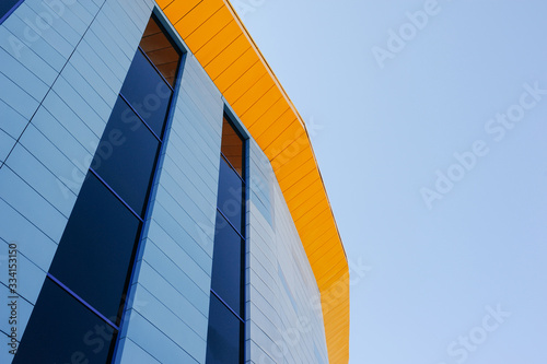 Stylish geometric blue glass building with the yellow roof in the background of the bright blue sky