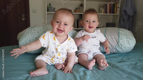Two cute fraternal twins sisters laughing and having fun on bed at home