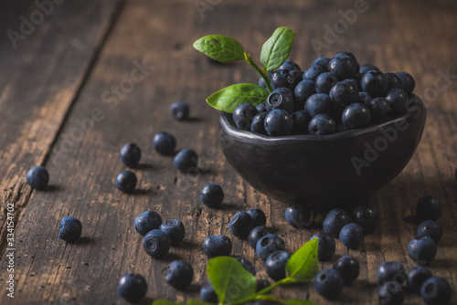 Clay bowl with organic, wild forest blueberries on a rustic wooden table.