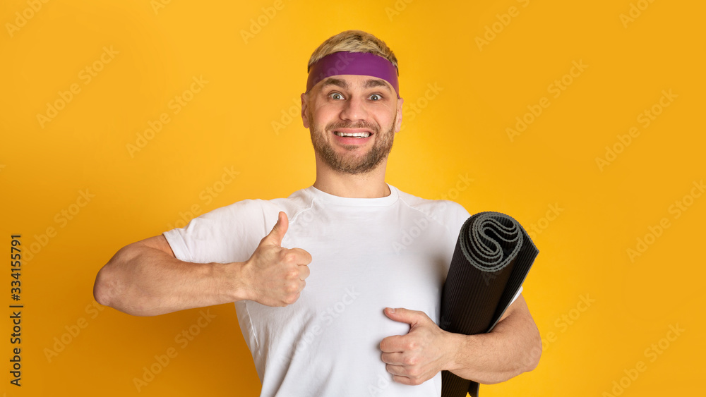 Smiling man with sports mat showing thumb up Smiling man with sports mat showing thumb up