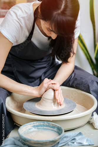 Brunette woman in an apron working on the potter's wheel