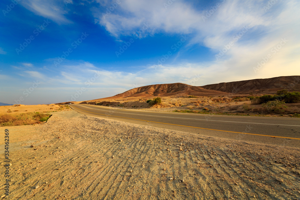 Road with car in a mountains in desert at sunset