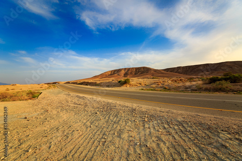 Road with car in a mountains in desert at sunset