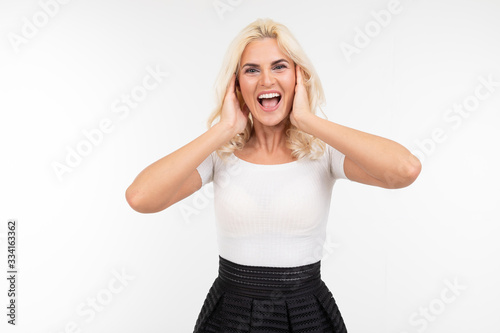 blond woman in a white t-shirt covers her ears with her hands because of noise on a white clean background