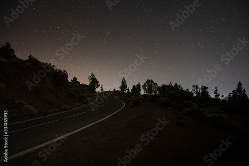 Empty night road on an island. Stars illuminate mountains and forest. Sun is rising. 