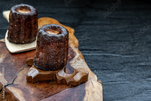 Cannelés (Canelés) de Bordeaux Recipe is a small pastry with rum and vanilla on a wooden plate.