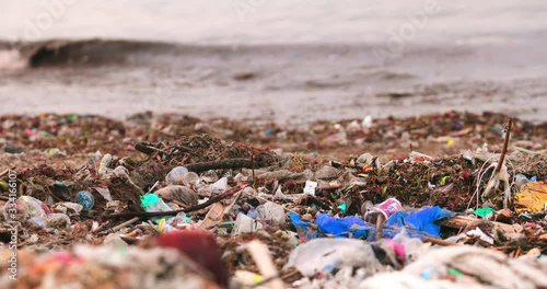 Plastic trash and garbage dumped on dark sand of the beach and floating on the surface of the ocean water. Environmental and water pollution problem concept. Marine pollution killing wildlife.