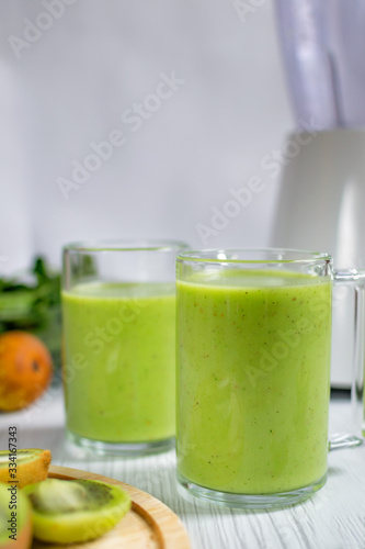 Green smoothie in glass with pear, spinach, kiwi and avocado on white wooden table. Copy space. 