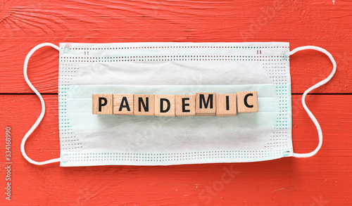 PANDEMIC. The word pandemic arranged from wooden letters on a protective mask and a red table.