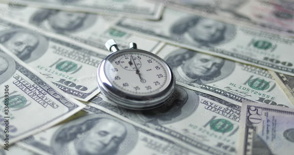 The stopwatch lies on the dollars. Time is money concept. The stopwatch lies on the dollars. Time is money concept.
