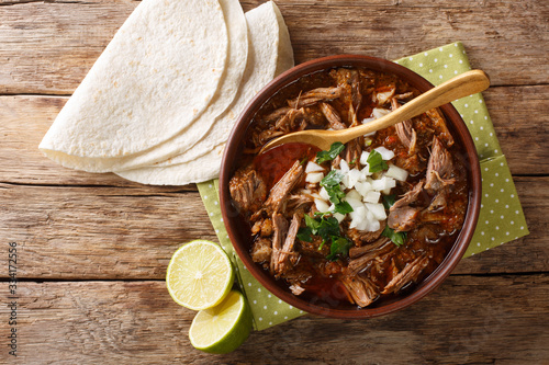 Mexican style slow cooked beef stew Birria de Res served with lime and tortilla closeup in a bowl. Horizontal top view photo