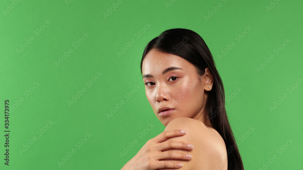 Fototapeta premium Beautiful woman portrait, beauty on green background, Asian woman standing half-turned holding her shoulder and looking at camera