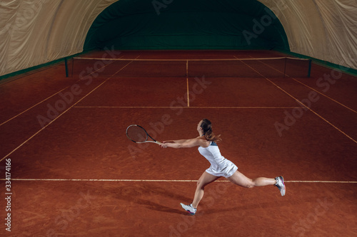 Young caucasian professional sportswoman playing tennis on sport court background. Training, practicing in motion, action. Power and energy. Movement, ad, sport, healthy lifestyle concept. High angle. © master1305