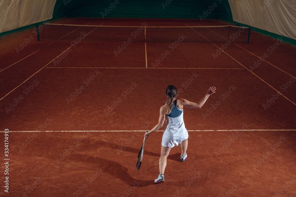 Young caucasian professional sportswoman playing tennis on sport court background. Training, practicing in motion, action. Power and energy. Movement, ad, sport, healthy lifestyle concept. High angle.