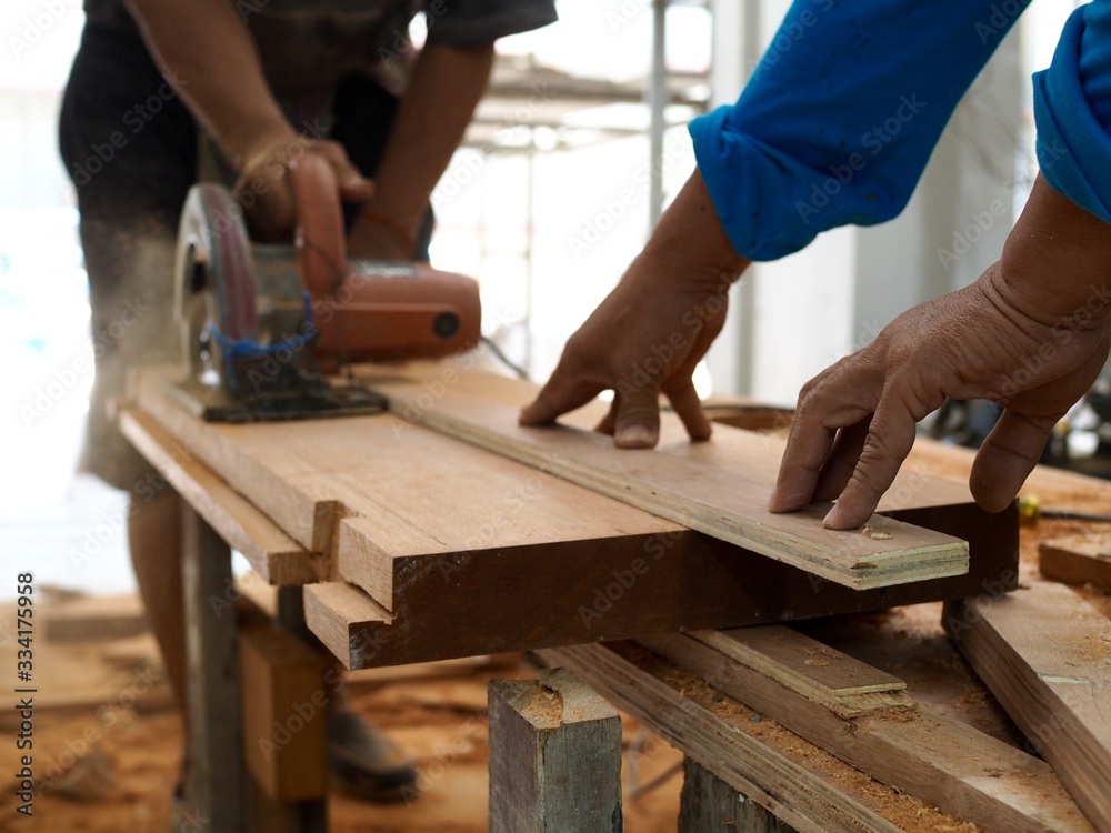 The hand of a man was helping to hold the wood to not move ,the carpenter to cut wood to make furniture. The hand of a man was helping to hold the wood to not move ,the carpenter to cut wood to make furniture.